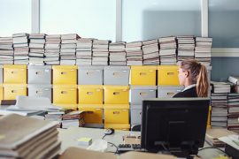 Imagem de uma mulher em um escritório cheio de arquivos empilhados