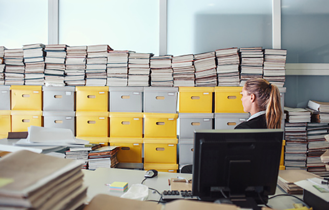 Imagem de uma mulher em um escritório cheio de arquivos empilhados