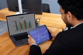 Pessoa de negócios olhando para gráficos financeiros em notbook e tablet