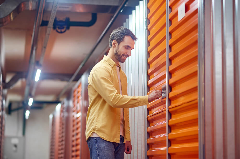corredor de self storage com box fechados e uma pessoa abrindo um deles com a chave