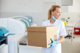 A imagem mostra uma doutora transportando uma caixa com itens médicos